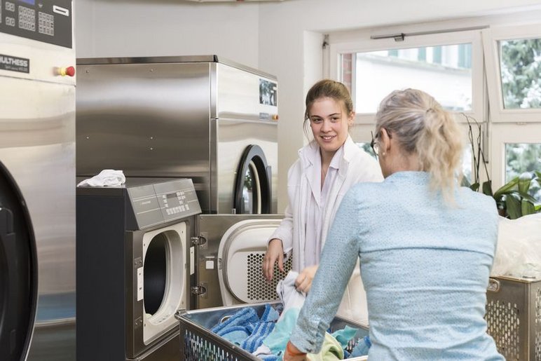 Aufnahme Berufsbildung-1. Arbeitsmarkt-Facility Services-Waschküche - Ausbilderin mit Lernender an der Wäschetrommel