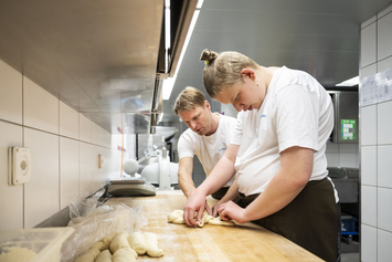 Berufsbildungsangebot-Bäckerei-Bäckermeister und Lehrling schwenken Teigg