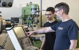 Aufnahme Berufsbildung-Metallwerkstatt-Ausbilder erklärt Lernenden wie man eine Maschine programmiert